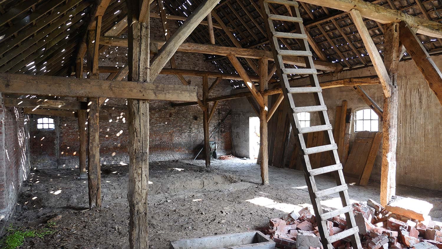 Intérieur de la grange avant travaux : charpente dégradée, sol en terre et gravats
