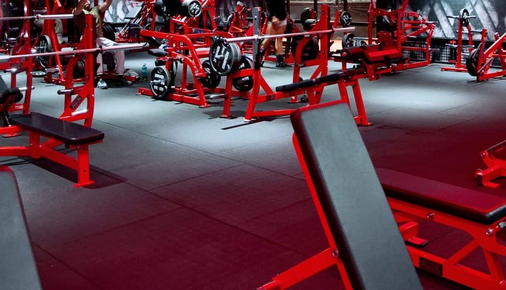 Plateau de musculation aux bancs et machines rouges, dans un ancien garage transformé en salle de sport à Décines-Charpieu