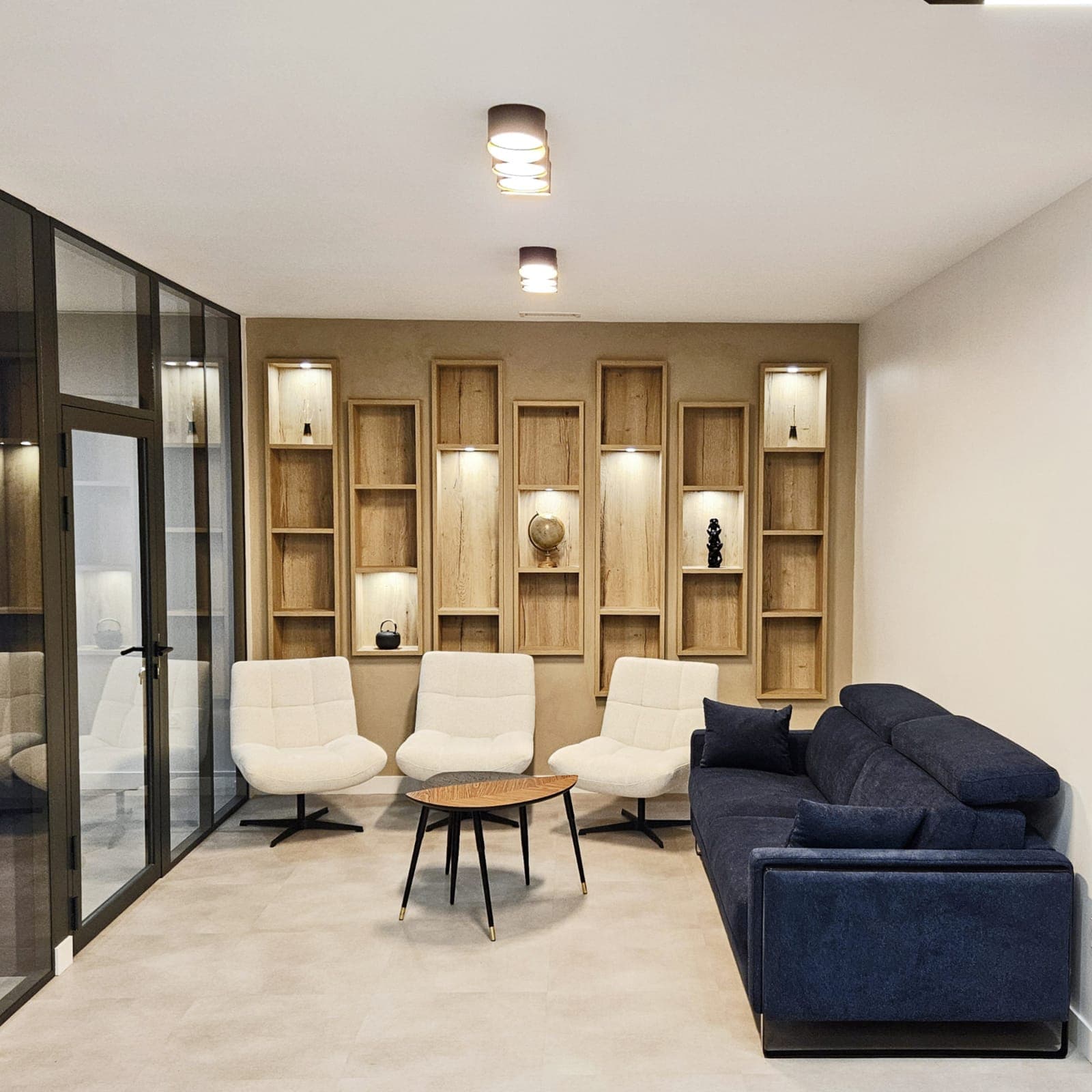 Espace d'accueil avec niches bois rétroéclairées, fauteuils blancs et cloison vitrée, dans des bureaux aménagés à Archamps