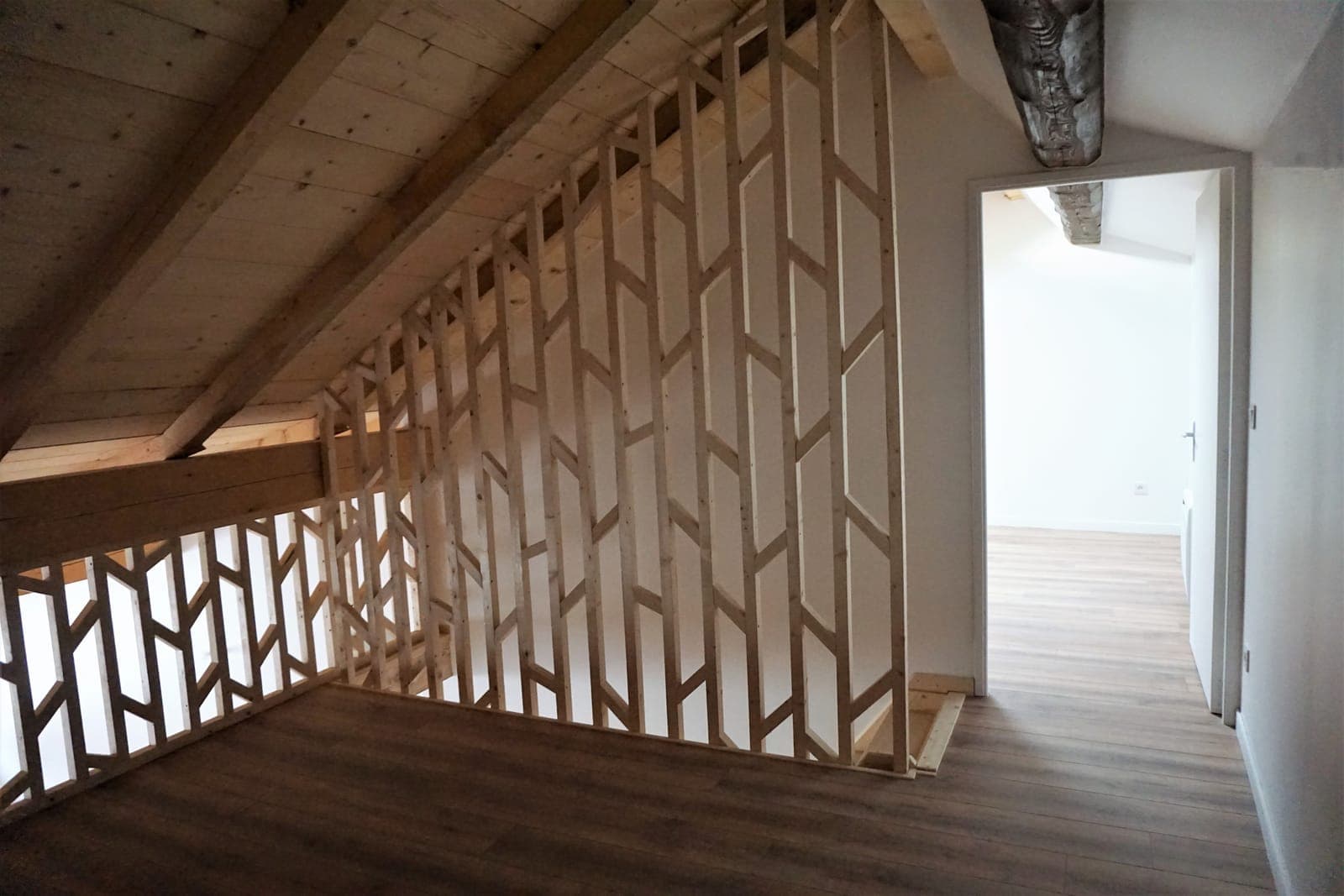 Garde-corps en claire-voie de bois à motif géométrique dans un appartement de l'immeuble réhabilité à Seyssel