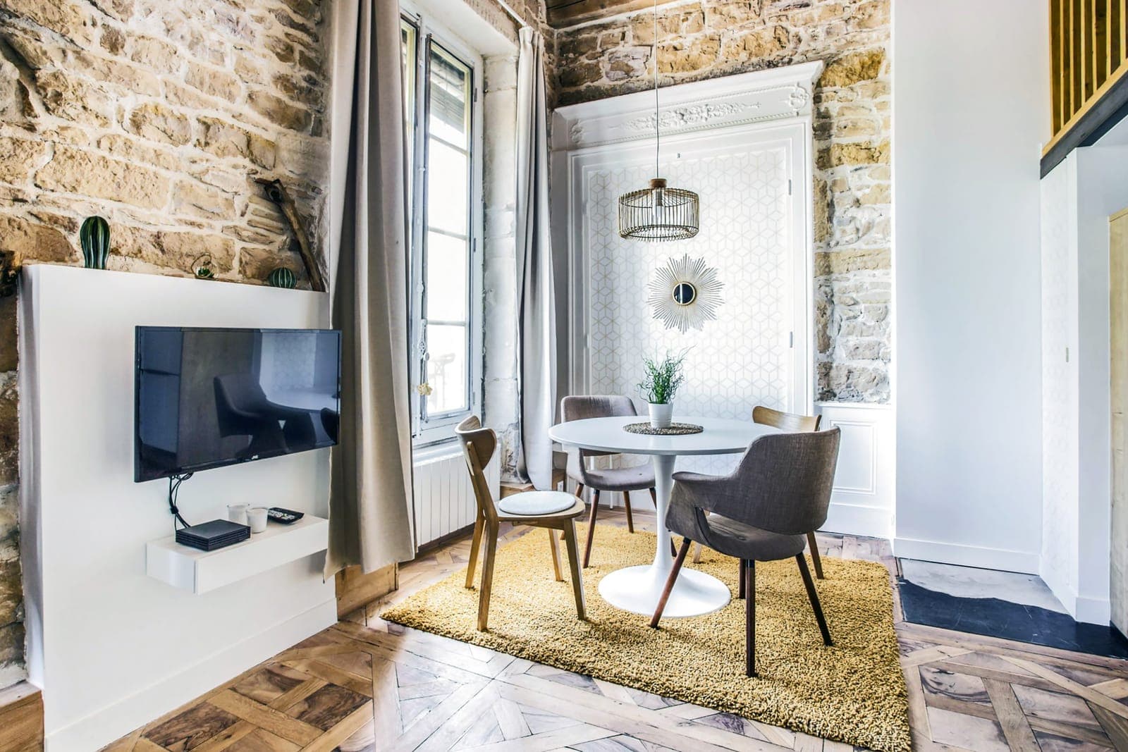 Séjour lumineux avec table ronde blanche, mur de pierre et poutres apparentes, dans une location saisonnière sur les quais du Rhône à Lyon