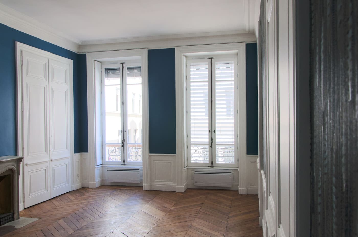 Pièce aux murs bleus avec hautes fenêtres à volets intérieurs et parquet, dans un appartement rénové à Bellecour, Lyon 2e