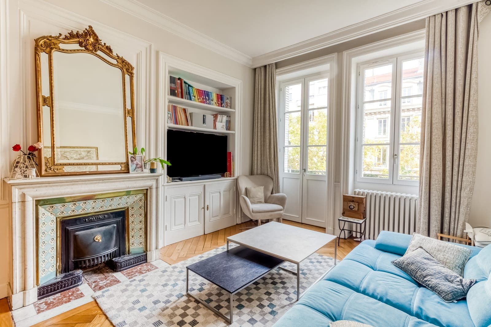 Salon haussmannien avec cheminée en marbre, miroir doré, bibliothèque et parquet, dans un appartement restructuré à Lyon 7e