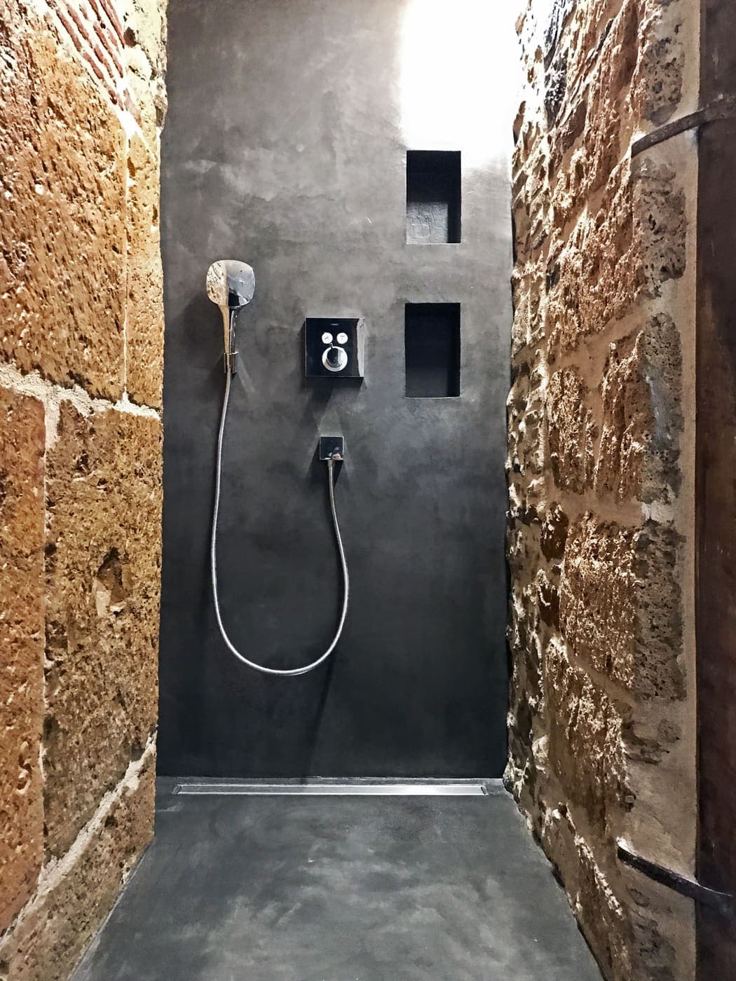 Douche à l'enduit minéral noir entre deux murs de pierre apparente, dans un appartement rénové à Bellecour-Hôtel Dieu, Lyon