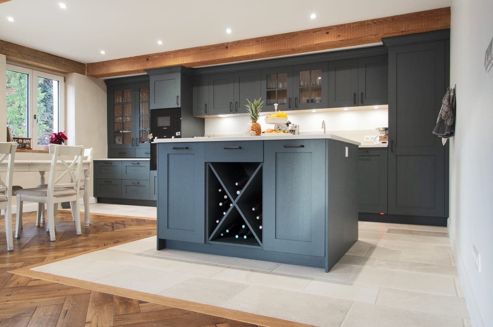 Cuisine sur mesure bleu ardoise avec îlot central sous poutre bois, dans une grange en pisé rénovée à Saint-Vulbas