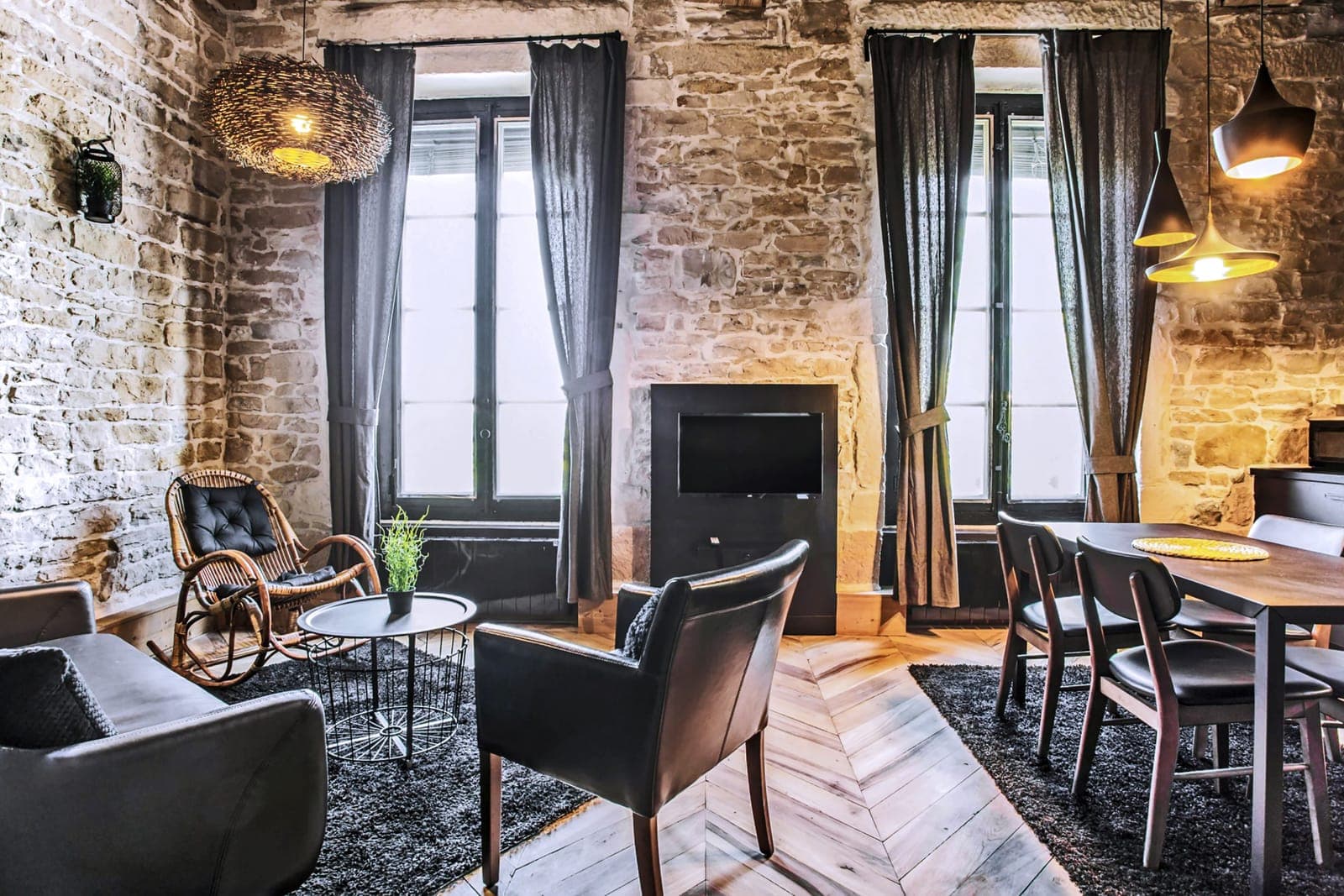 Séjour aux murs de pierre et rideaux noirs, fauteuils cuir et parquet pointe de Hongrie, dans un appartement sur les quais du Rhône à Lyon