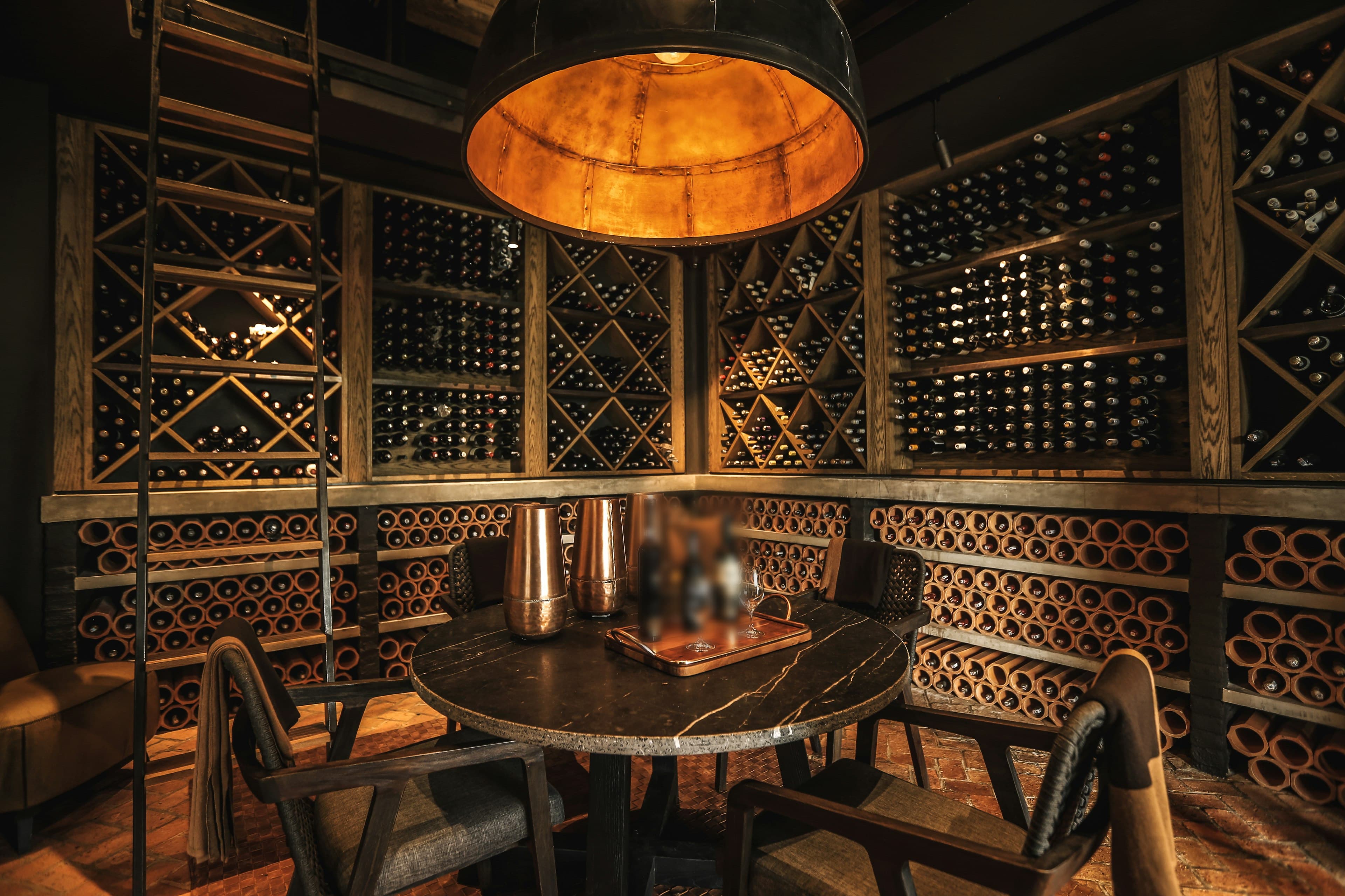 Cave à vin intimiste aux casiers en bois, table ronde en marbre sous une grande suspension cuivrée