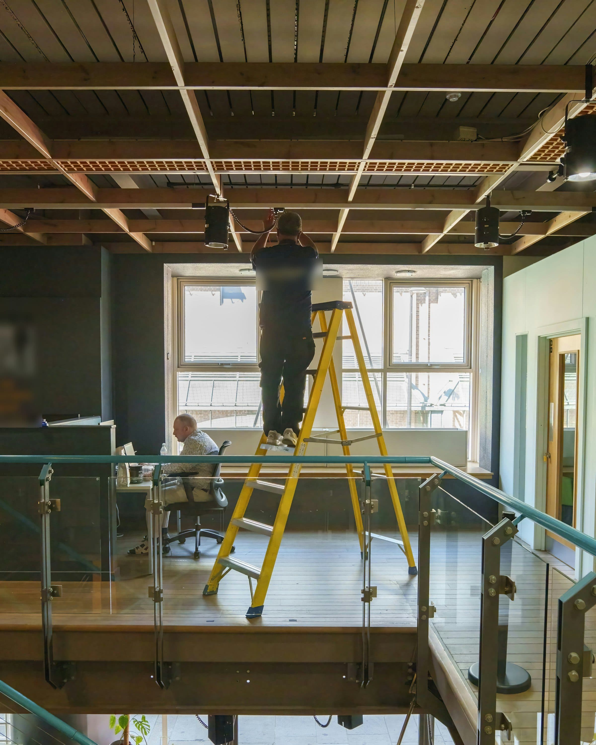 Électricien sur un escabeau qui intervient au plafond pendant que l'équipe continue de travailler