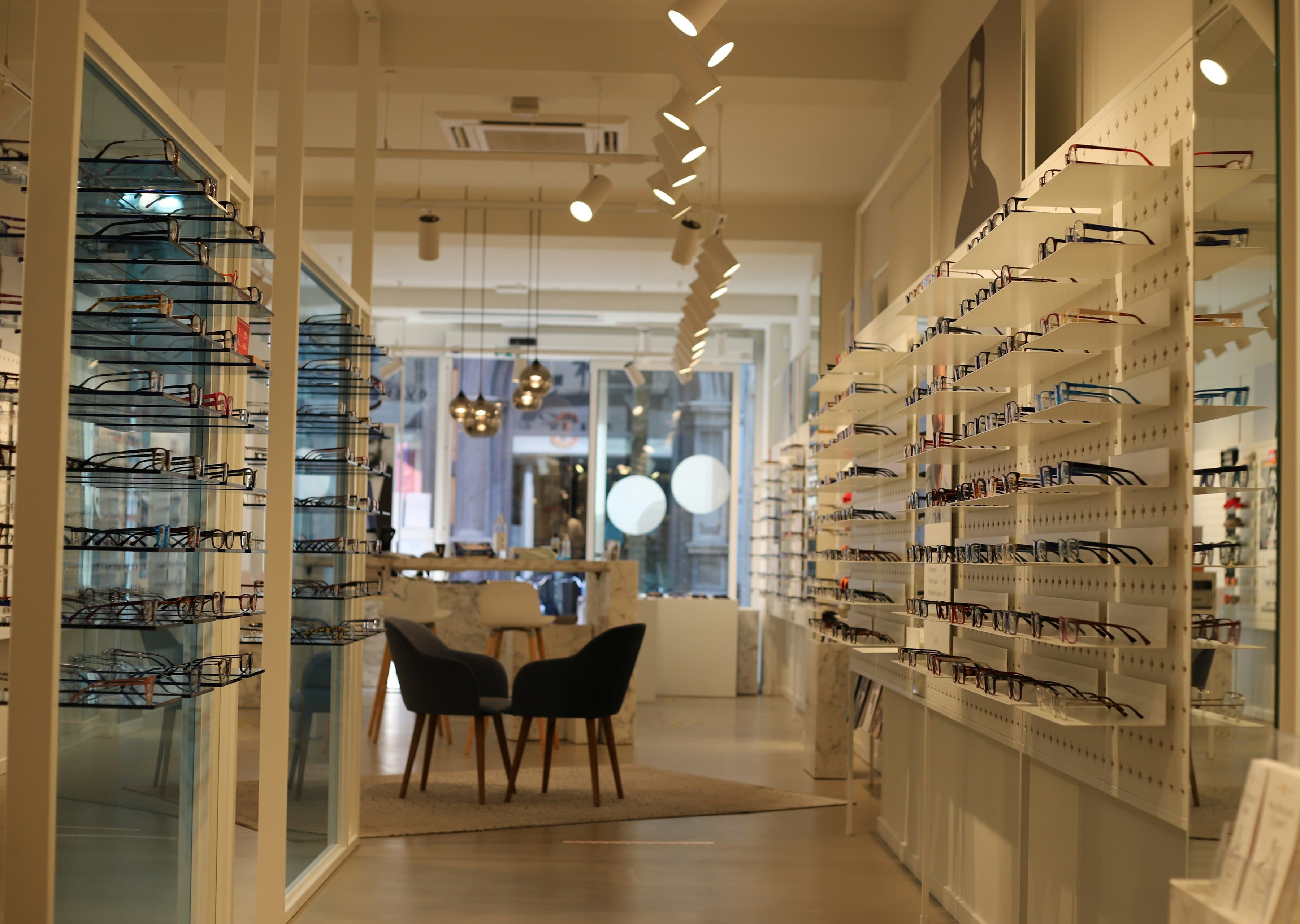 Boutique d'opticien claire, murs de présentoirs à lunettes et coin conseil avec fauteuils