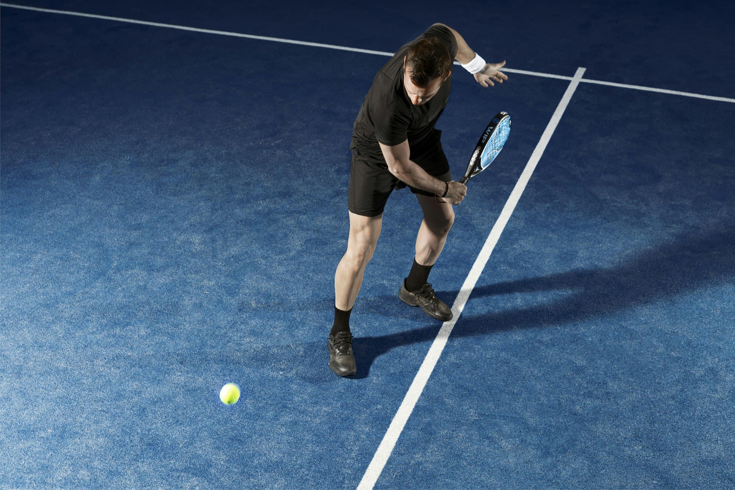 Joueur de padel qui frappe la balle sur un court bleu