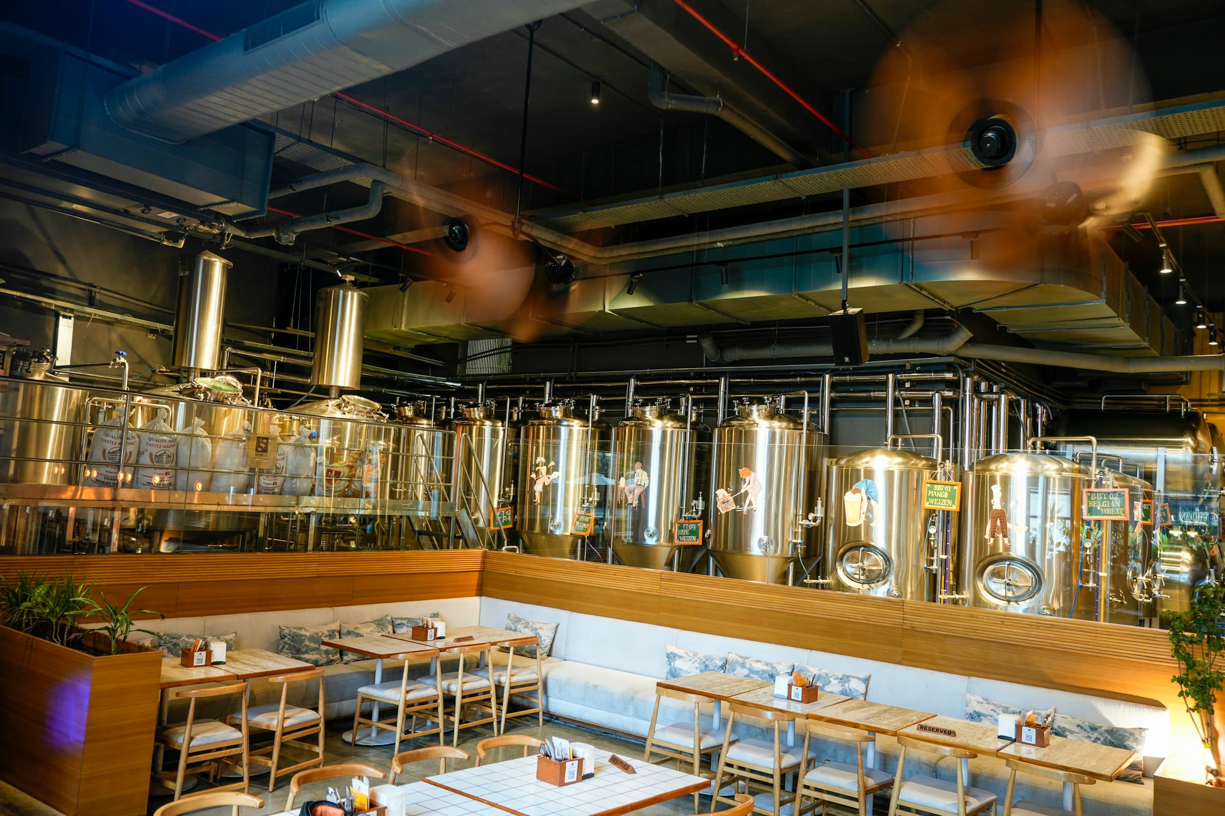 Brasserie aux tables de bois face aux cuves de brassage en inox