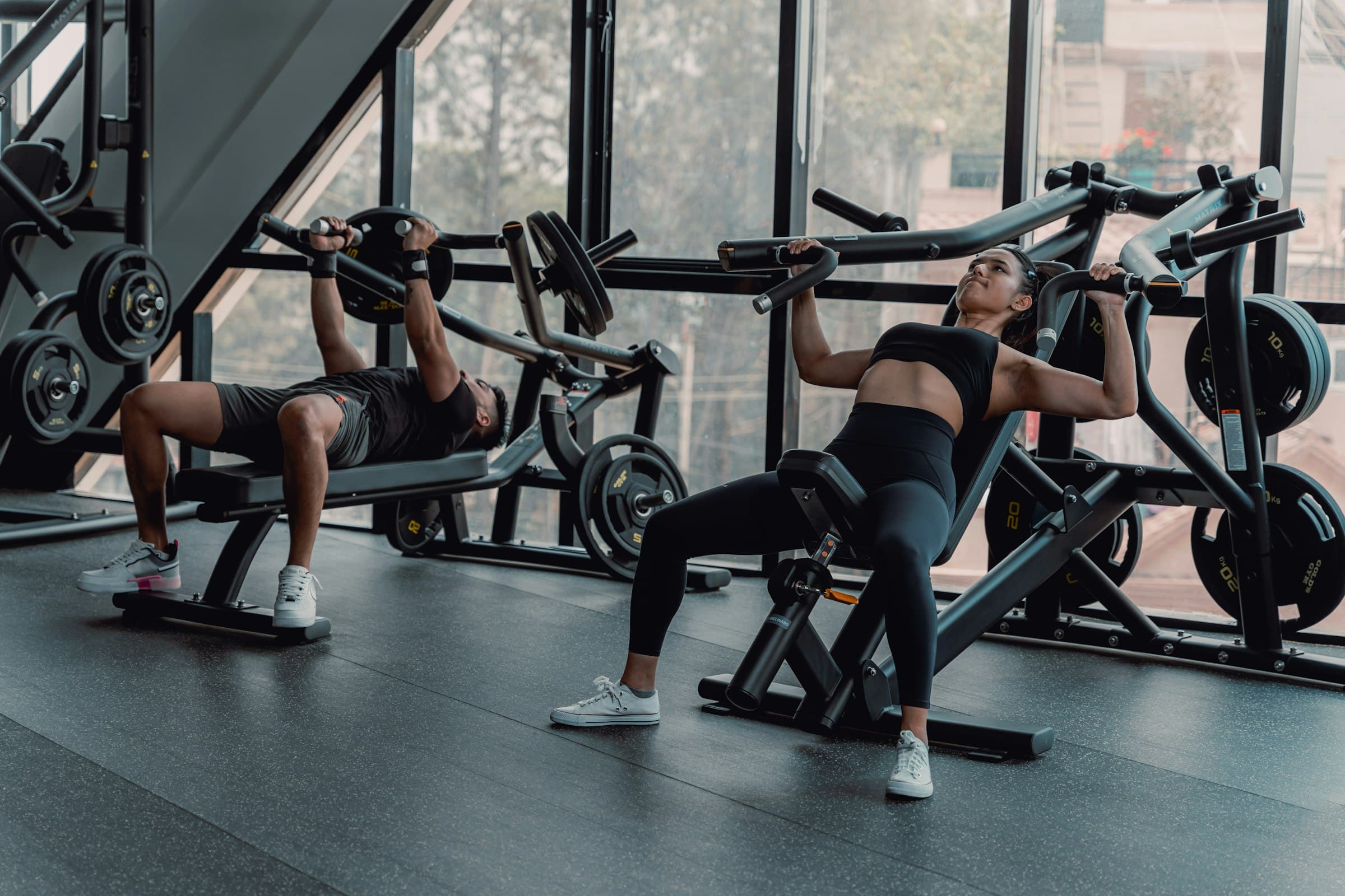 Deux adhérents qui s'entraînent sur des machines de musculation devant une baie vitrée