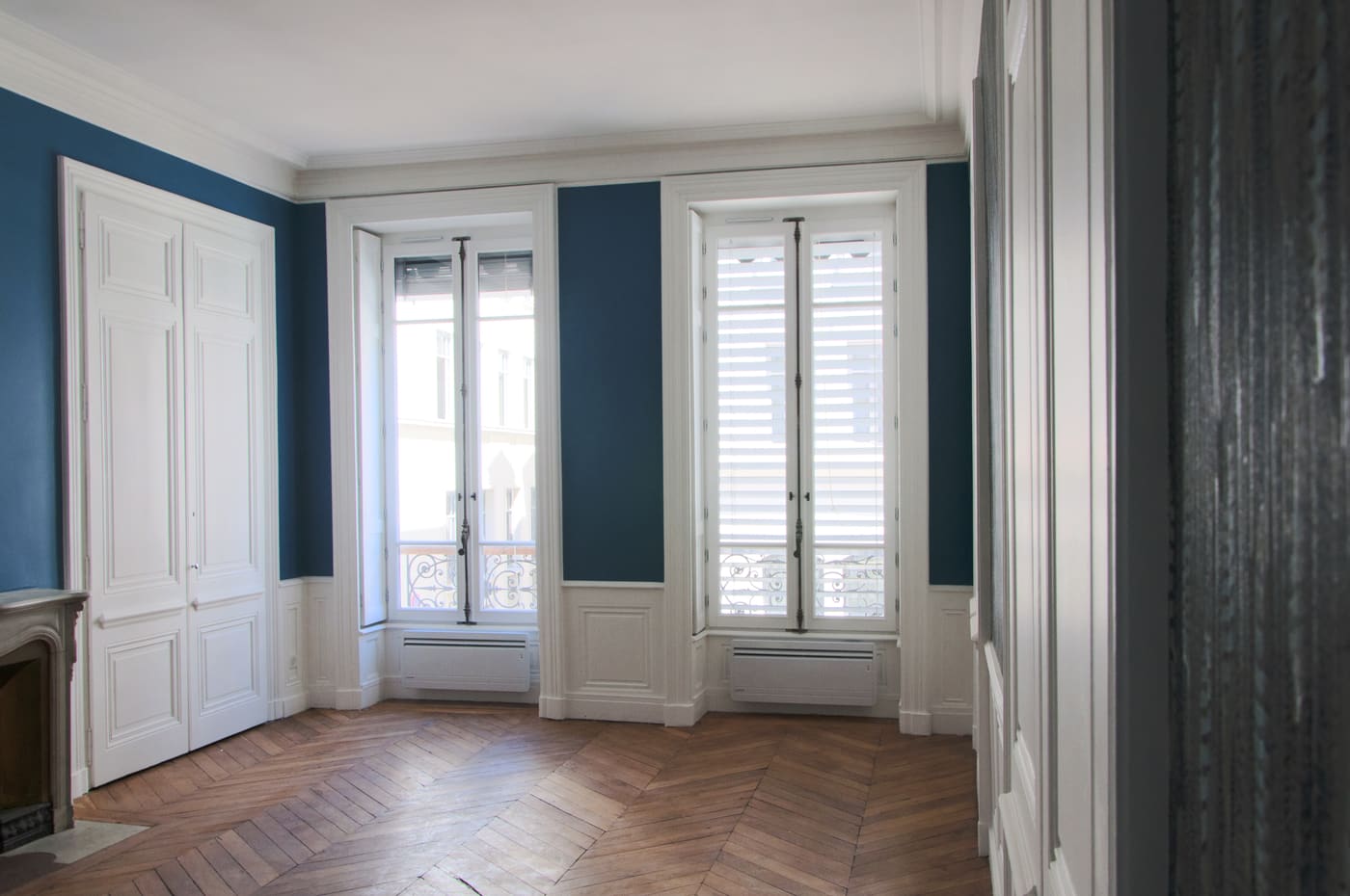 Pièce aux murs bleus avec hautes fenêtres à volets intérieurs et parquet, dans un appartement rénové à Bellecour, Lyon 2e