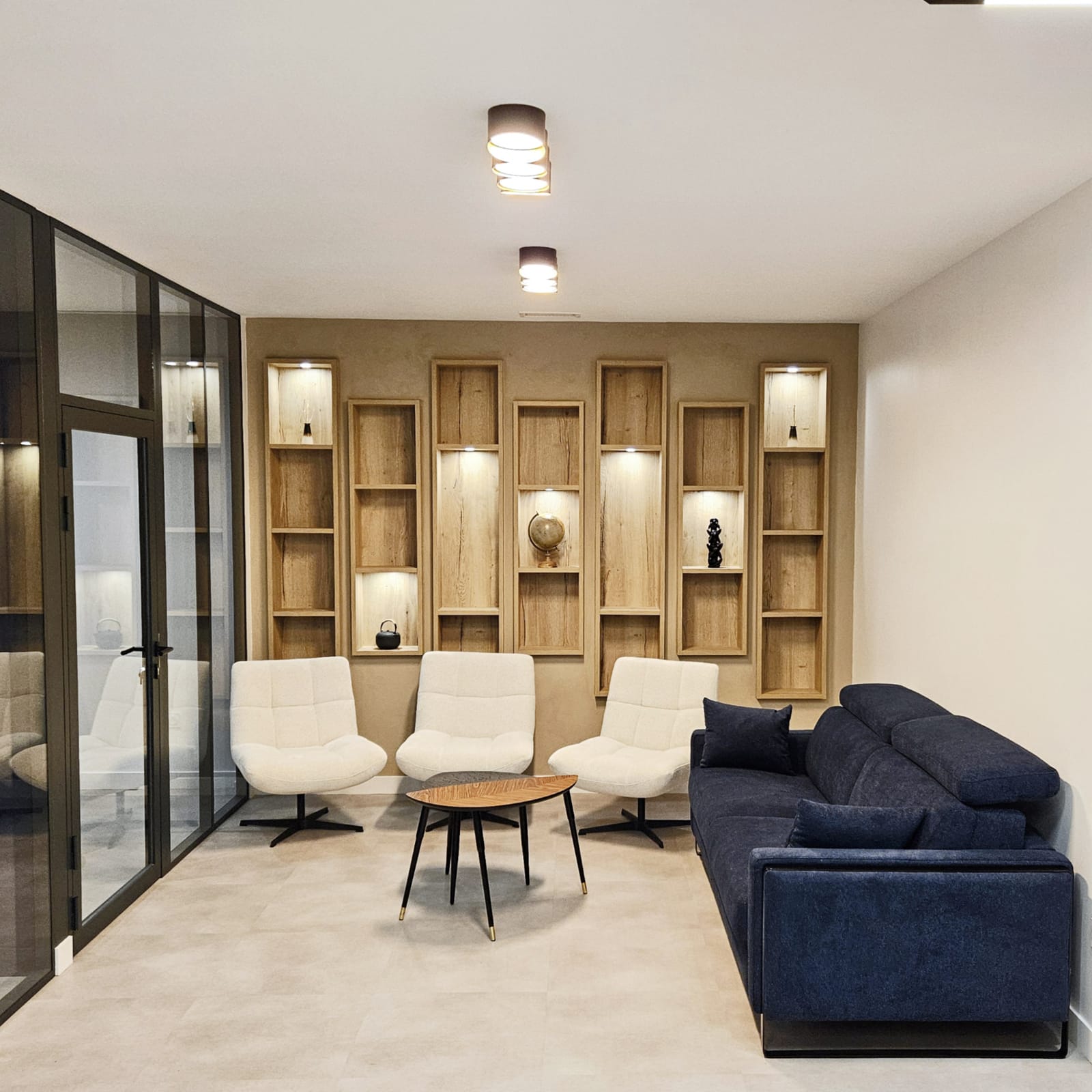 Espace d'accueil avec niches bois rétroéclairées, fauteuils blancs et cloison vitrée, dans des bureaux aménagés à Archamps