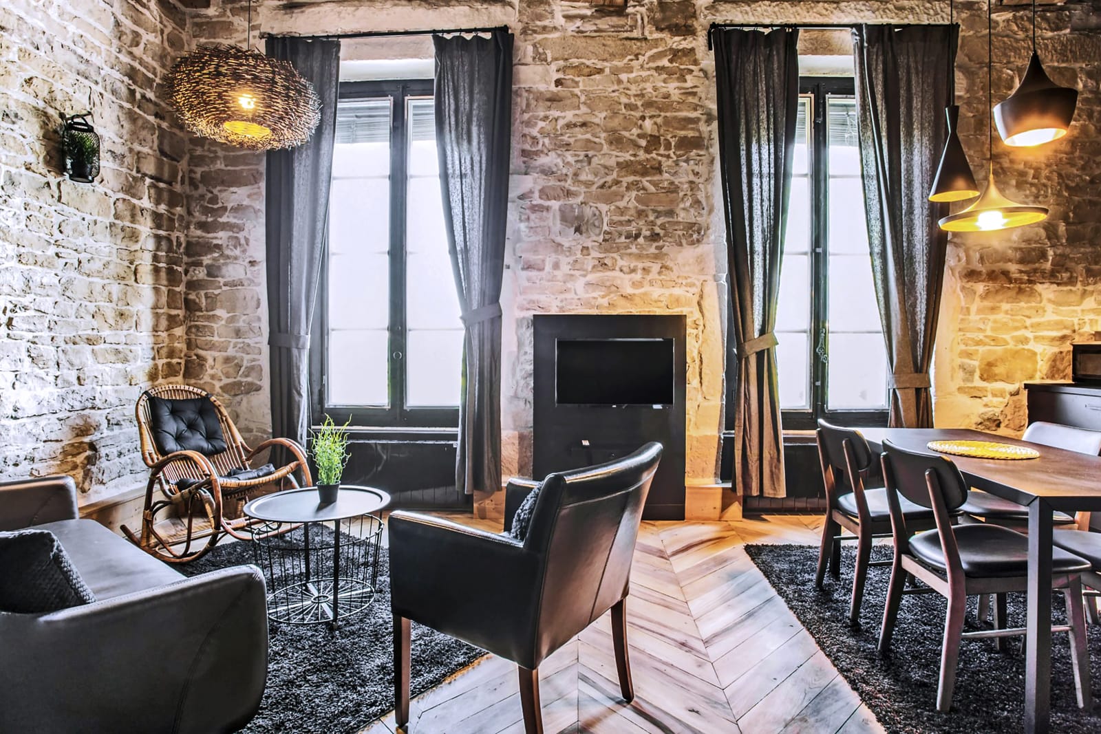Séjour aux murs de pierre et rideaux noirs, fauteuils cuir et parquet pointe de Hongrie, dans un appartement sur les quais du Rhône à Lyon