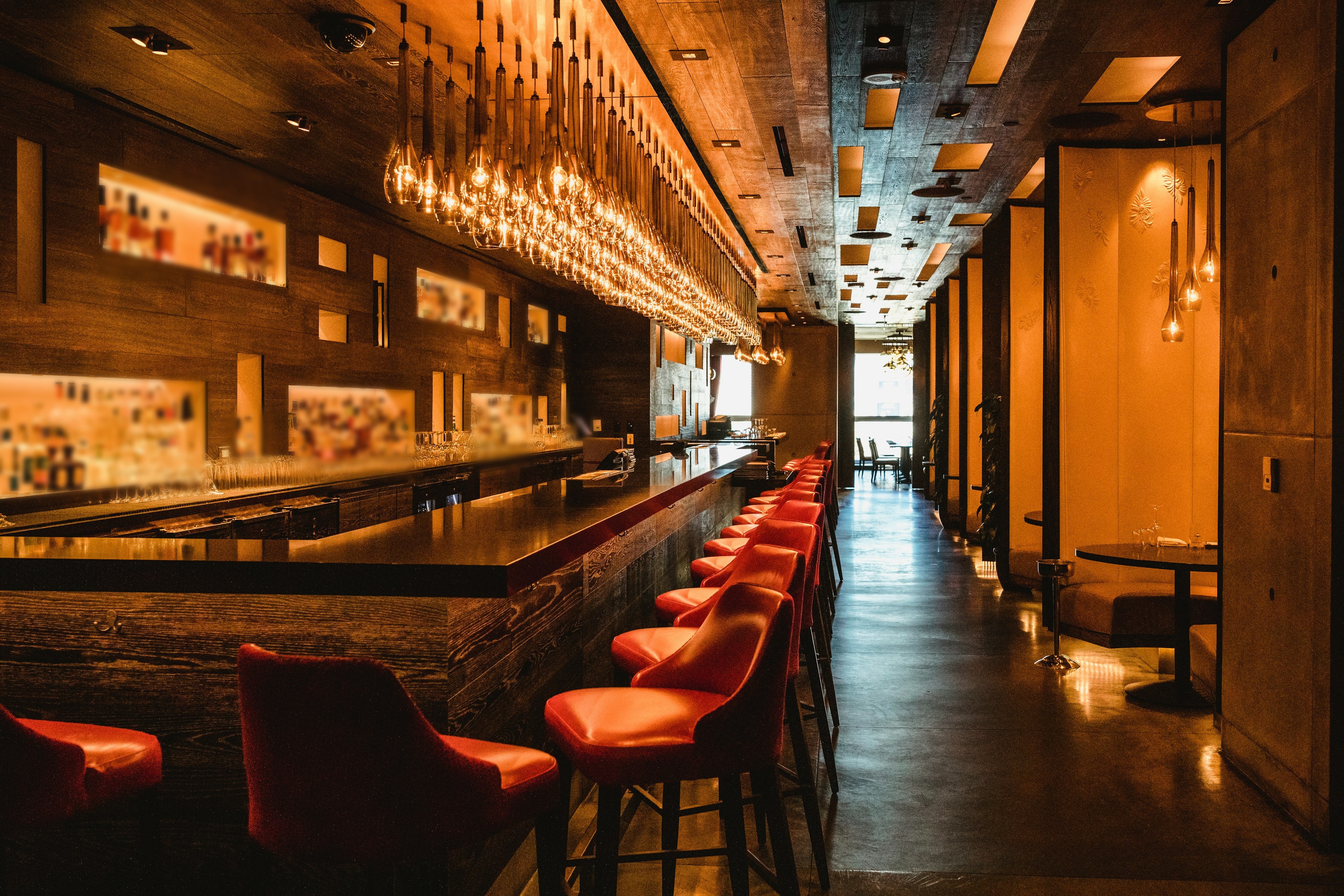Long comptoir de bar en bois sombre, tabourets rouges et rideau de suspensions en verre ambré