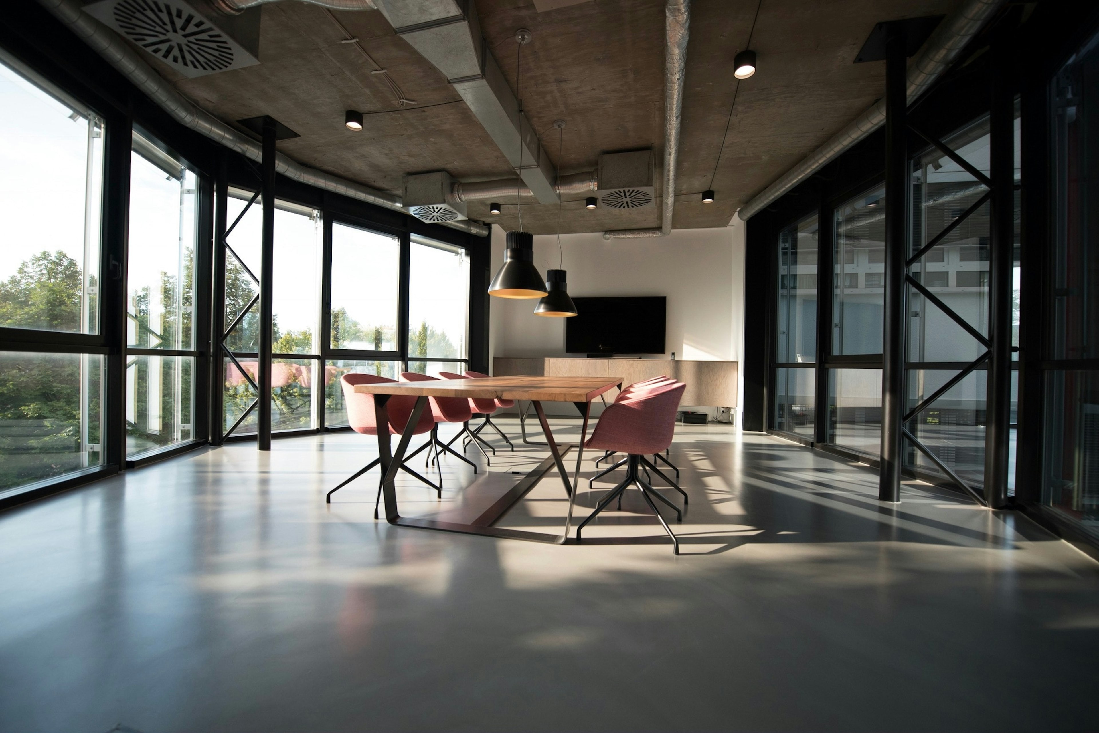 Plateau de bureaux baigné de lumière, grande table de réunion sous plafond béton et façade vitrée sur la verdure